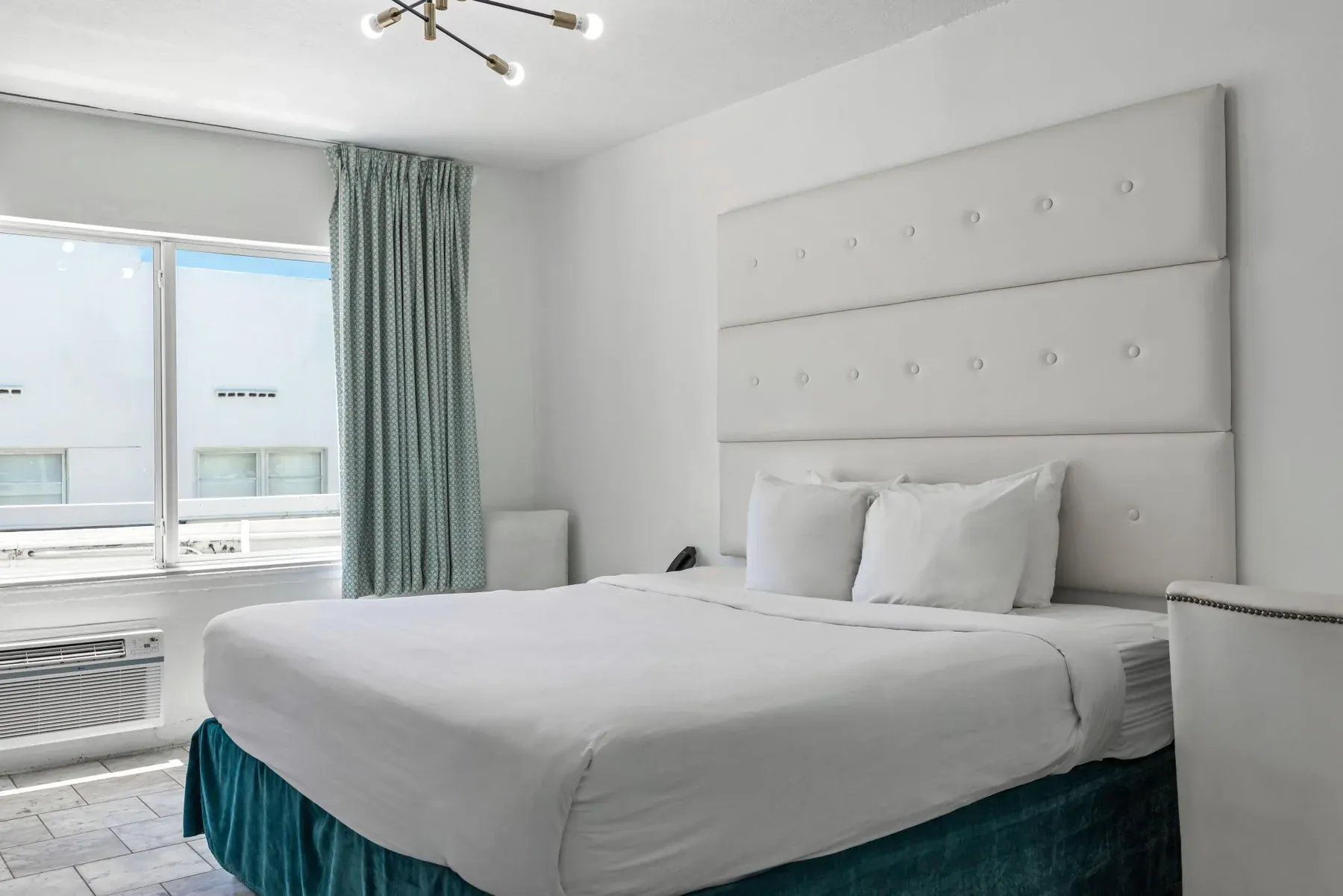The king bed head-on, buttoned white headboard and a teal bed skirt