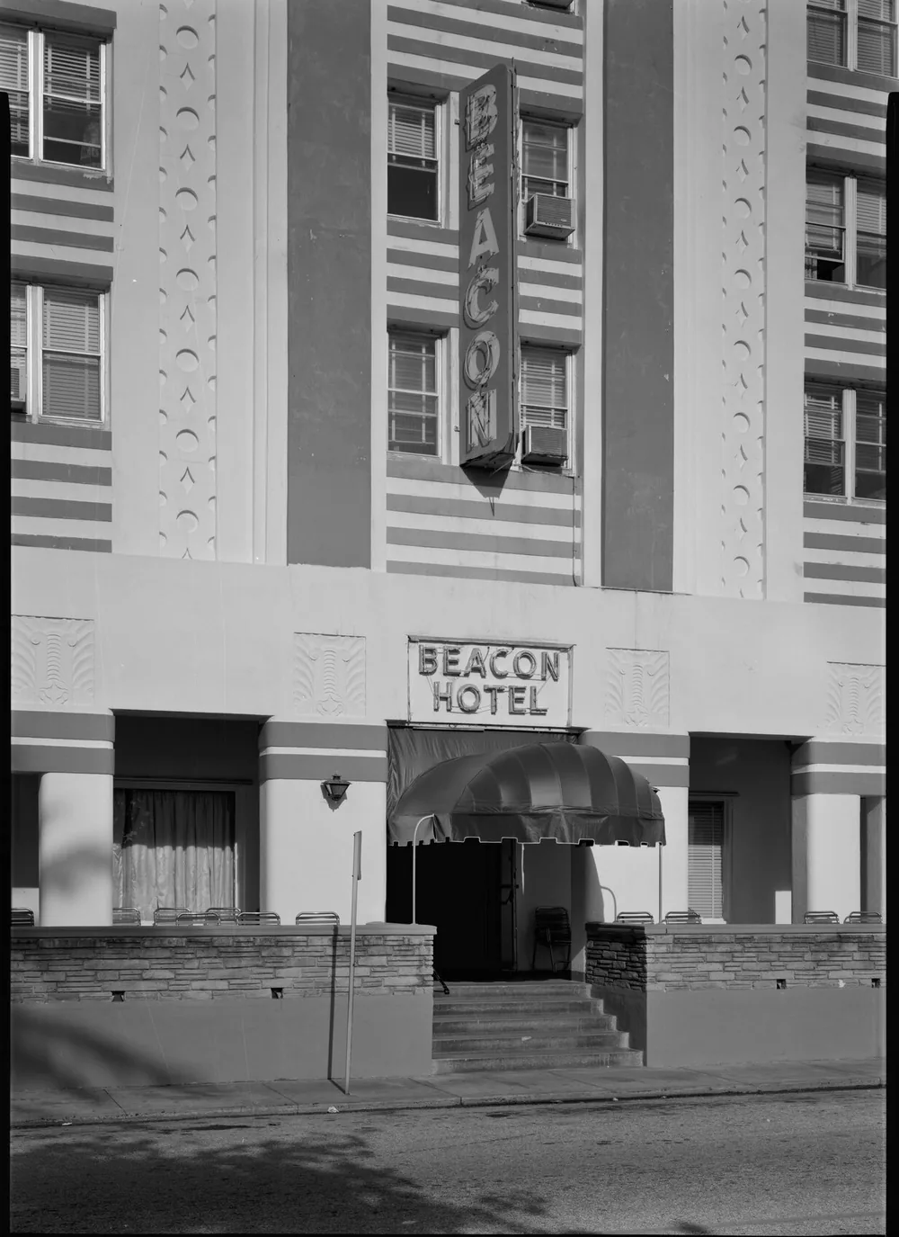 Archival photograph of the Beacon Hotel entrance on Ocean Drive, showing the vertical BEACON neon sign and the Deco entrance canopy